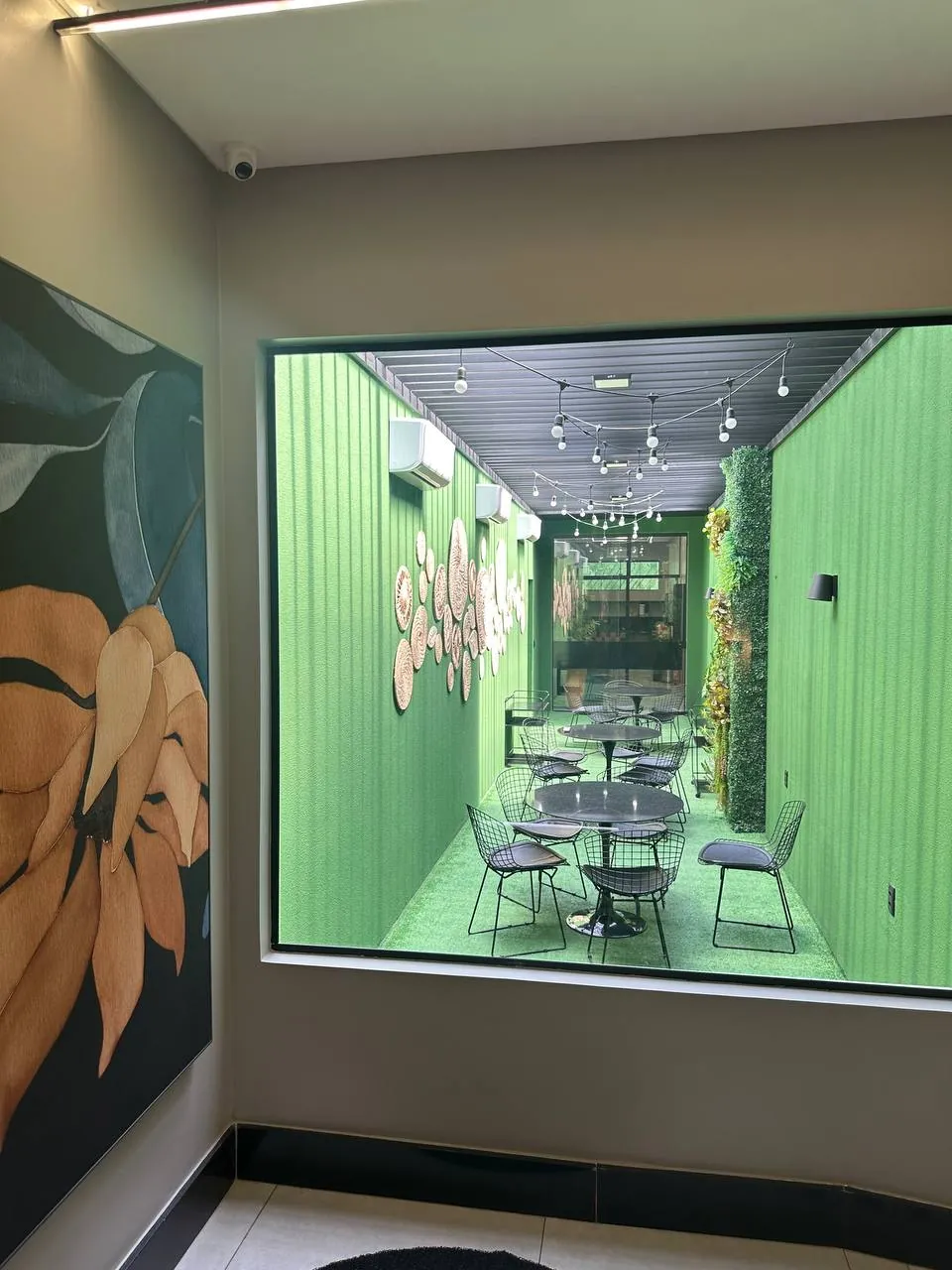 Circulação interna do My Office com painel artístico floral e vista para o pátio verde de convívio