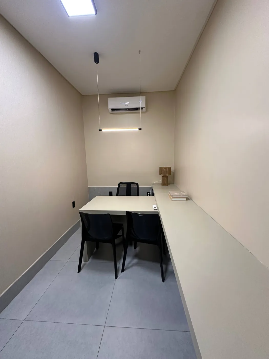 Sala privativa do My Office com bancada clara em L, duas cadeiras e iluminação suspensa