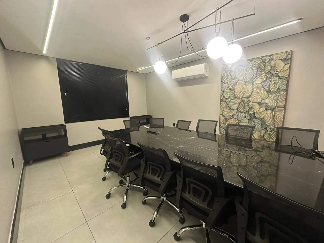 Sala de reunião do My Office com mesa longa em pedra escura, dez cadeiras executivas, painel de TV e obra de arte